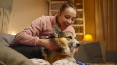 happy joyful smiling woman lying on bed in bedroom and playing with her cute funny welsh corgi dog. friendship with pets, games together and leisure. domestic animals in peoples life