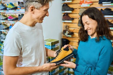 Büyüleyici kadın satış danışmanı sunumu erkek müşteriye ayakkabı mağazasında mükemmel bir çift ayakkabı.