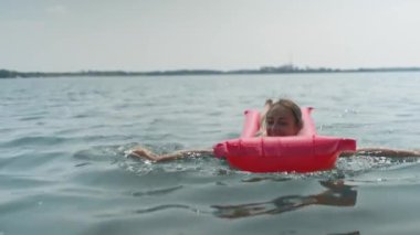 Genç ve güzel bir kadın gölde yüzen pembe şişme bir yatakta eğlenirken gülüyor.