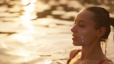 Kaygısız bir kadın, altın gün batımında huzur ve rahatlık içinde sırtüstü yüzüyor.