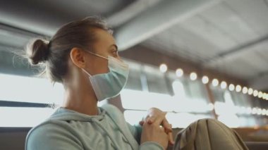 Tıbbi maske takan genç bir kadın klinikte bekliyor, sağlık ve bulaşıcı hastalıklar hakkındaki endişelerini yansıtıyor. Ayarlama, tıbbi bakım, güvenlik ve önleme temalarının altını çiziyor.