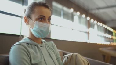 Koyu renk gözlü ve bronz tenli güzel bir kadın klinik lobisinde koruyucu bir maske takıyor. Sahne sağlık endişelerini, güvenliği ve bulaşıcı hastalıkların önlenmesini simgeliyor.