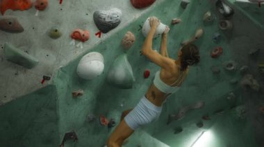 Spor kıyafetli güçlü kız spor salonundaki renkli yapay duvara tırmanıyor aşırı hareketliliğe odaklanmış kayaları tutuyor. Gençlik, eğlence ve eğitim konsepti.