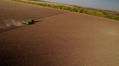 Tarım alanında çalışan yeşil traktör kuru toprak ekip biçiyor ve gün batımında hava sineması manzarası seyrediyor. Tarım sektörü konsepti. Küçük tarım kavramı. Çekici disk harrow saban alanı üzerine