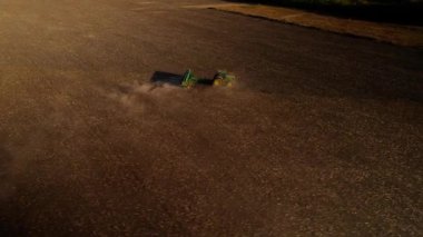 Gün batımında tarlada çalışan traktörün hava gözlem dronu, altın ışık. Tarım sektörü konsepti. Küçük tarım kavramı. Çekici disk harrow tarlayı sürüyor. Sonbahar, hasat ve tohum ekme