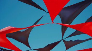 Mavi gökyüzü arka planında rüzgarla dalgalanan kırmızı ve siyah üçgenin soyut görüntüsü. Yaz kampı ya da plaj kulübü dekorasyonu, canlı renkler