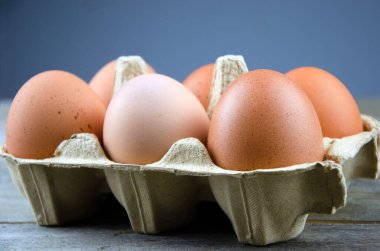 Altı kahverengi tavuk yumurtası ahşap masada, mavi arka planda.