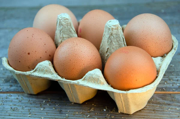 Six brown chicken eggs in box on wooden table