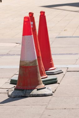 Üç turuncu trafik konisi bir sıra halinde kaldırımda, güneşli bir günde