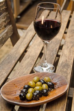 Bir kase karışık zeytin ve bir bardak kırmızı şarap dışarıdaki ahşap masada.