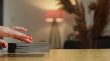 Kırmızı tırnaklı bir kadın güverteden tarot kartlarını alır ve masanın üzerine serer.