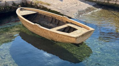 Tahta kayık halatla bağlanmış. Küçük limandaki berrak suya bağlanmış. Çevre ve güneş ışığını yansıtıyor..