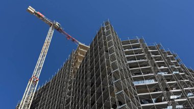  Budva, Karadağ-11 Nisan 2025: Gökyüzü altında, iskelelerle çevrili kıvrımlı bir ön cephe ve yakınlardaki bir kule vinci ile modern bir gökdelen.