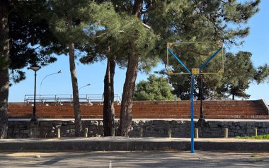  Budva, Karadağ-11 Nisan 2025: Yıpranmış bir basketbol potası, arka planda grafiti kaplı basamaklarla ağaçlarla çevrili bir alanda tek başına duruyor. Yüksek kalite fotoğraf