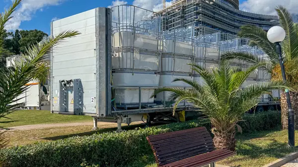 Budva, Karadağ - 18 Mayıs 2025: Palmiye ağaçlarıyla çevrili katlanmış dönme dolap kabinleri taşıyan nakliye karavanı