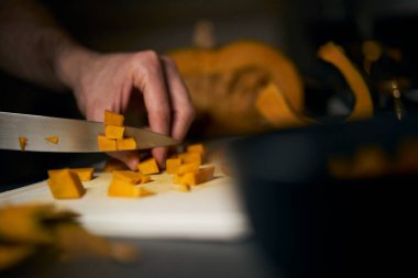 Adam havalı, yuvarlak bir balkabağını koyu arkaplanı olan küçük parçalara ayırıyor. Loş ışıklandırmalı karanlık stil Cadılar Bayramı ve sonbahar için harikadır. Kesik turuncu balkabağı parçalarını kapat.