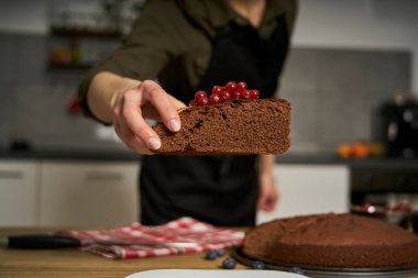 Aşçılığa tutkusu olan bir kadın ev mutfağında böğürtlenli ve kırmızı üzümlü bir dilim çikolatalı pasta süsler..