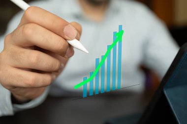 Beyaz bir stil tutan adam dijital olarak yansıtılan bir bar tablosunu işaret ederken veya çizerken, büyümeyi, ilerlemeyi ve finansal başarıyı sembolize eder. Resim görsel olarak veri analizi, iş stratejileri ve ekonomi kavramlarını temsil etmektedir.