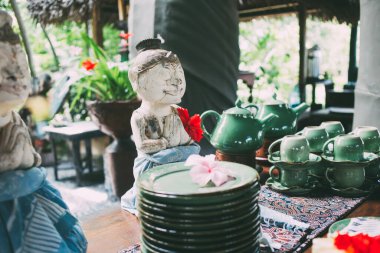 Budist egzotik heykeller ve yeşil seramik çay ve tabak servisi dinlenme yerinde tropikal çiçeklerle masaya kuruluyor. 