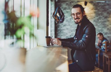 Uzaktan kumandalı mutlu erkek işçinin portresi kameraya gülümserken aynı zamanda proje için uygulama ve dizüstü bilgisayarda 4G kablosuz bilgi araştırması yapıyor.