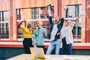 Gündelik giyinmiş öğrencilerin portresi kameraya gülümserken el ele tutuşuyor. Şehir merkezinde iş birliği yaptıktan sonra kameraya poz veren farklı gençlerin mutlu bir şekilde el ele tutuşması.
