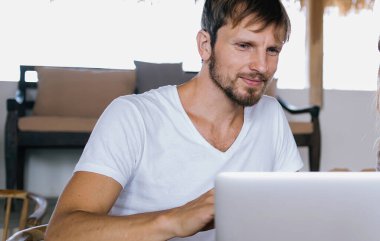 Laptop kullanan yakışıklı bir adam ve kafedeki ahşap masada oturup kahvenin tadını çıkarırken elinde defter tutan güzel bir kadın.