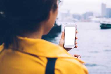 Kötü bir günde Hong Kong 'da şehir körfezinin kıyısında duran, elinde beyaz cep telefonu olan, tanınmayan bir kadının arka görüntüsü.