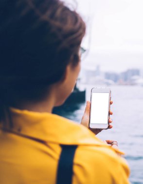 Kötü bir günde Hong Kong 'da şehir körfezinin kıyısında duran, elinde beyaz cep telefonu olan, tanınmayan bir kadının arka görüntüsü.