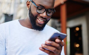 Milenyum adamı akıllı telefonuyla internette sohbet ediyor şehir ortamında dışarıda vakit geçiriyor, cep telefonundan ücretsiz internet bağlantısına bağlı neşeli hipster blogcu bildirimi okuyor.