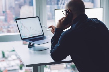 Yetişkin, profesyonel bir adamın bilgisayarını işaret ederken ofisteki pencereye karşı çalışan bilgisayarını göstermesi.