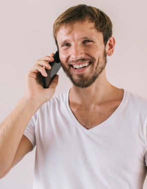 Boş tişörtlü, marka etiketli, boş tişörtlü mutlu bir erkek. Reklam alanı yakınlarındaki akıllı telefon iletişiminin tadını çıkarıyor. Taşınabilirlik yaşam tarzı.