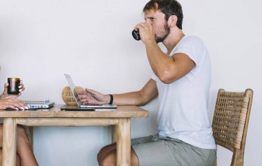 Yetişkin, yakışıklı, sakallı, günlük giysiler giymiş, kafeteryada beyaz arka planda giyinmiş neşeli, güzel bir kadının önünde meyve suyu içen bir erkek.