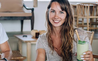 Genç, güzel bir kadın egzotik kokteylden zevk alıyor ve kameraya bakarken sakallı bir adam gündüz kafede dizüstü bilgisayarla oturuyor.