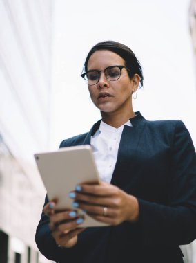 Gözlüklü, açık mavi manikürlü, iş kıyafetleri giyen, gündüzleri işe giderken tablet kullanan kadın girişimci.