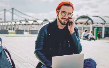 Modayı takip eden gülümseyen hippi portresi cep telefonu sohbetini dışarıda dizüstü bilgisayarla yapıyor, uluslararası öğrenci kameraya bakarak cep telefonu görüşmesi yapıyor.