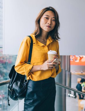 Halka açık yerlerde cep telefonu ve kahve ile poz veren güzel hippi kız portresi. Deri etekli ve sırt çantasıyla kameraya bakan modaya uygun giyinmiş kadın.