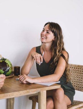 Yan bakışta kısa elbiseli, kısa elbiseli, çapraz bacaklı, beyaz gömlekli, akıllı telefonlu, gülümseyen genç bir kadın görülüyor. 