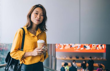 Halka açık yerlerde cep telefonu ve kahve ile poz veren güzel hippi kız portresi. Deri etekli ve sırt çantasıyla kameraya bakan modaya uygun giyinmiş kadın.