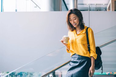 Hong Kong 'da kahve ve cep telefonuyla merdivenlerden aşağı inen sarı tişörtlü, siyah deri etekli ve sırt çantalı güzel, pozitif, güzel Asyalı kadın.