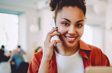 Mutlu Afrikalı bir kadın akıllı telefon cihazıyla arkadaşından bilgi almak ve ders hakkında danışmanlık yapmak için dizüstü bilgisayarda çalışmak için telefon konuşması yapan gülümseyen hippi kızın portresi.