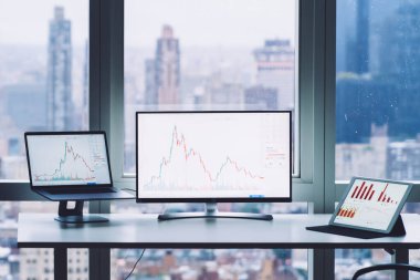 Masaüstünde cihazlarla çalışan çağdaş bir adam ve şehir arka planına sahip pencerenin önünde duran akıllı telefondan çağrı almak