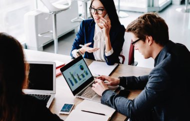 Profesyonel giyinmiş ofis çalışanları teknoloji ve kablosuz ağ kullanarak bilgi aramada işbirliği yapıyorlar. Erkek, internet üzerinden yazı yazarken kadın meslektaşı cep telefonuyla konuşuyor.