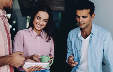 Neşeli çeşitli erkek ve kadınlar ofis içi iş günlerinde modern dokunmatik ped üzerinden komik web videoları izliyorlar, olumlu genç çalışanlar online iletişim için teknolojiyi kullanıyorlar.