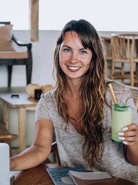 Genç, güzel bir kadın egzotik kokteylden zevk alıyor ve kameraya bakarken sakallı bir adam gündüz kafede dizüstü bilgisayarla oturuyor.