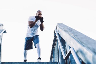 Spor kıyafetleri ve spor ayakkabıları giyen siyah kaslı eğitmenlerden şehir merdivenlerinin tepesinde duran ve sokak antrenmanı sırasında boks yapan