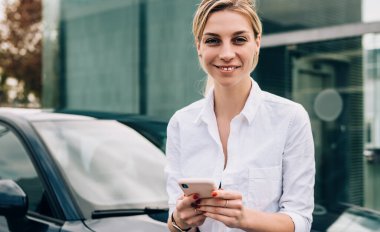 Neşeli, genç, sarışın kadın şoför. Sıradan kıyafetler giyip, akıllı telefondan sohbet ediyor. Sokakta siyah arabanın yanında dikilip kameraya bakıyor.