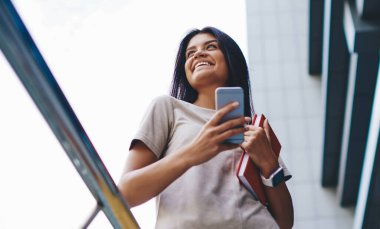 Boş zamanlarında şehir ortamlarında kitap ve akıllı telefonla gezen güzel, neşeli bayan öğrenci, dışarıda cep telefonuyla zaman geçiren 4G internet bağlantısından memnun olan mutlu kadın blogcu.
