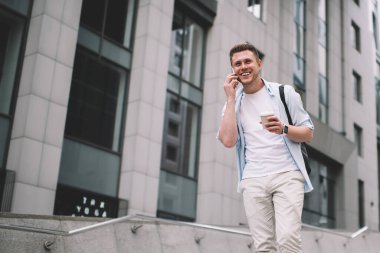 Havalı genç adamın elinde bir fincan kahve tutmasından ve şehir caddesinde yürürken cep telefonuyla mutlu bir şekilde konuşmasından