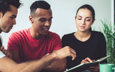 Gündelik giyinmiş zeki erkek ve kadın öğrenciler eğitim kitaplarından bilgi topluyor. Beyin fırtınası sırasında notlardan bilgi okuyan çok kültürlü erkekler ve kadınlar.