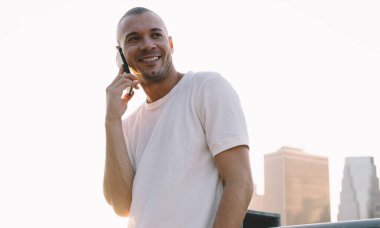 Aşağıdaki beyaz tişörtlü, kısa saçlı adamdan tırabzana yaslanmış ve telefonda gülümseyen.